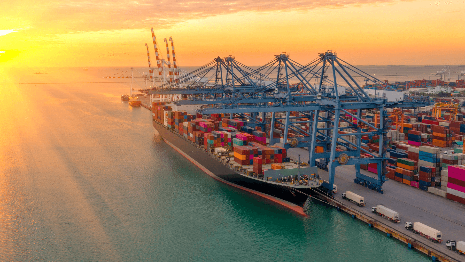 Loaded container ship of a shipping company at quay in large port with cranes at sunset.