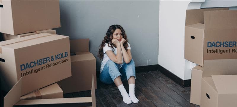 Young woman sits sadly among moving boxes – symbolic image of emotional stress caused by relocation depression.