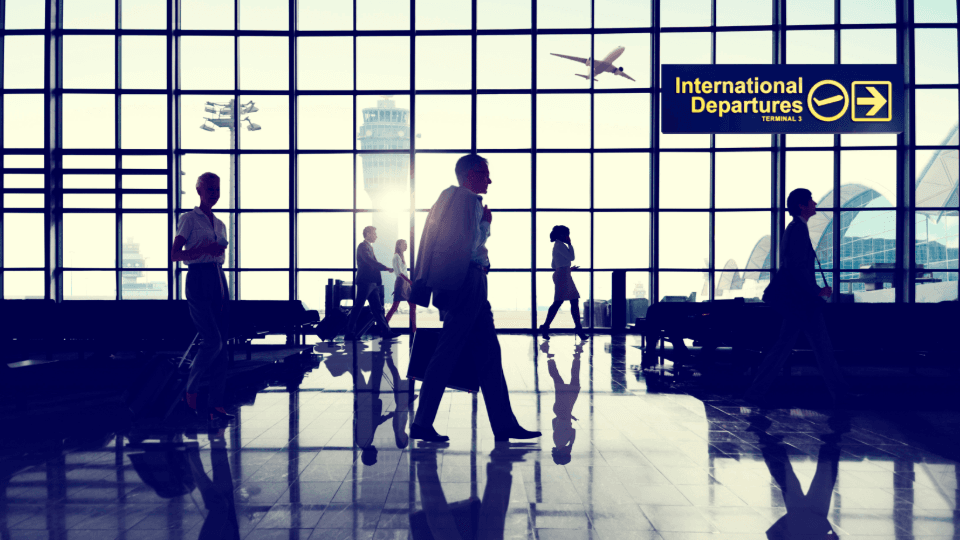 Silhouettes of travelers in a terminal by a large window with an "International Departures" (AOD) sign.