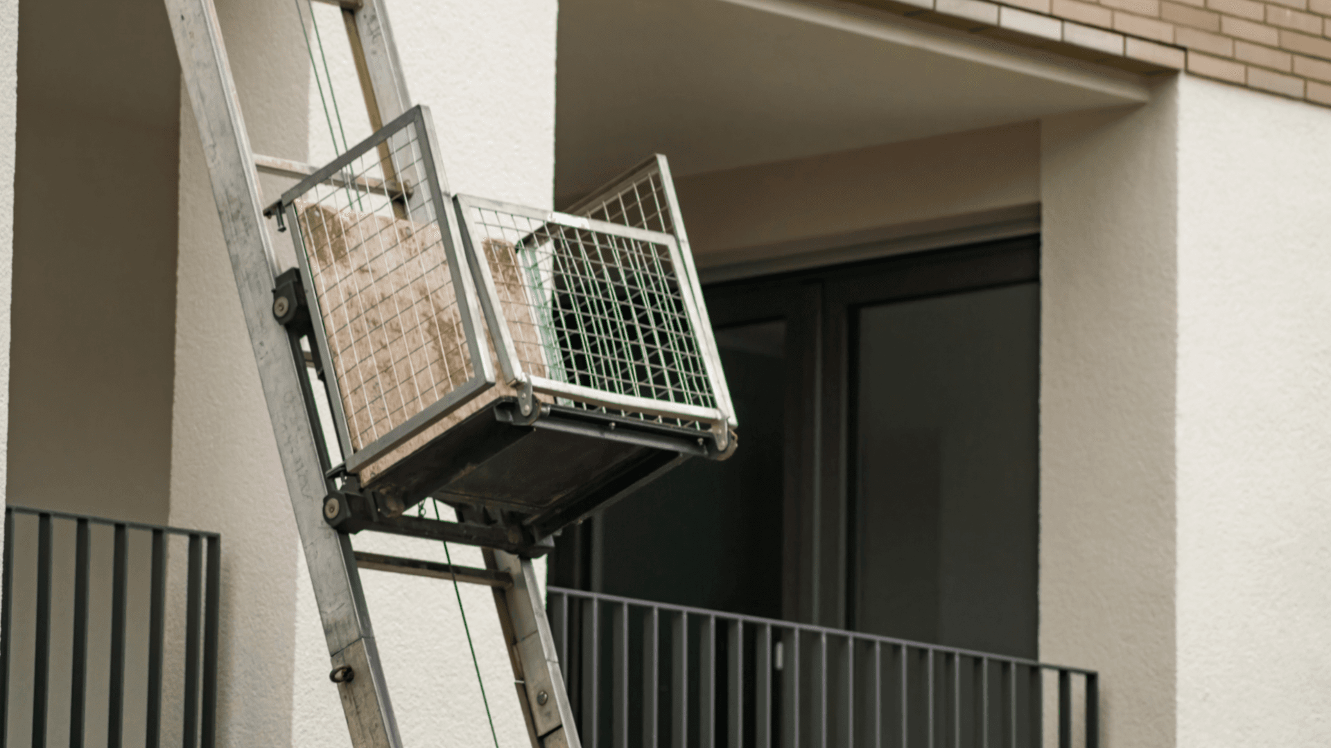 External lift with mesh platform carries a box up to a balcony of an apartment building.