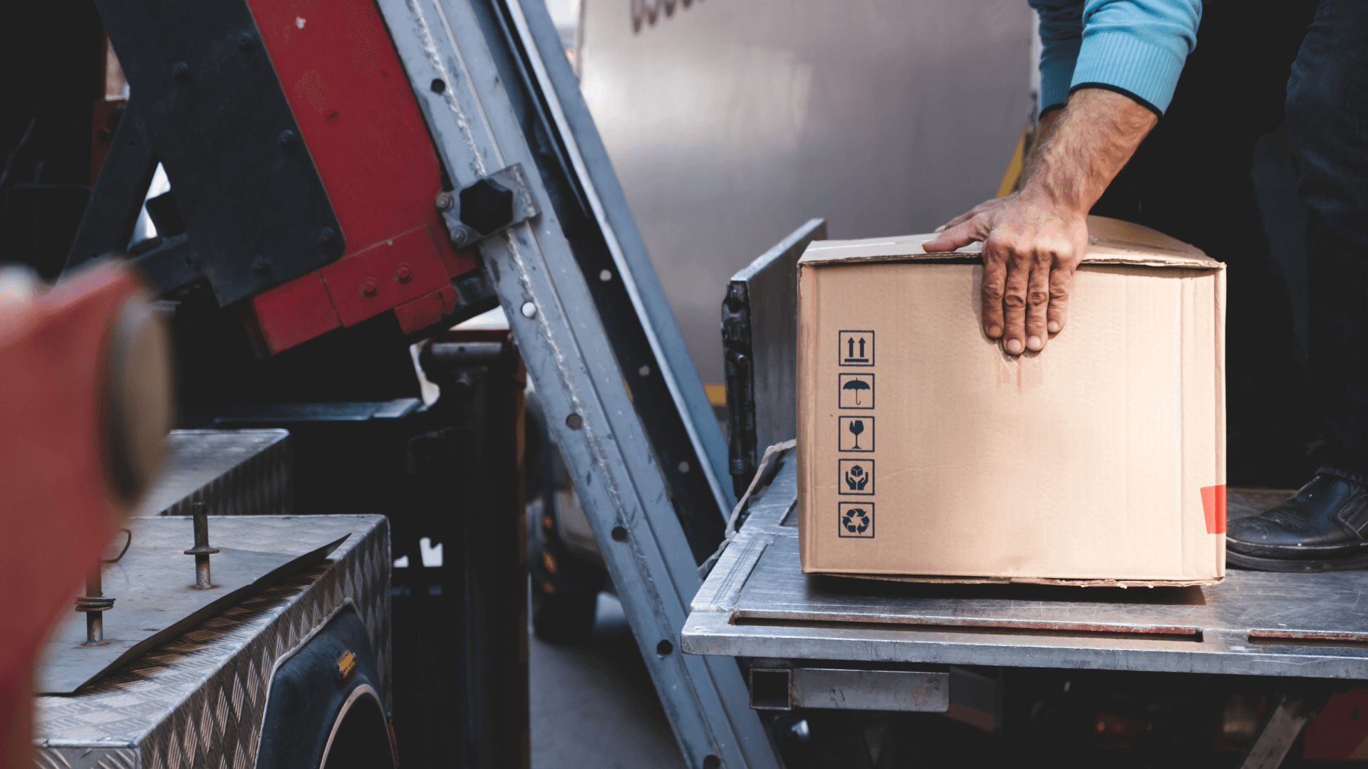 Mitarbeiter platziert Umzugskarton auf Außenaufzug-Plattform am Lkw.