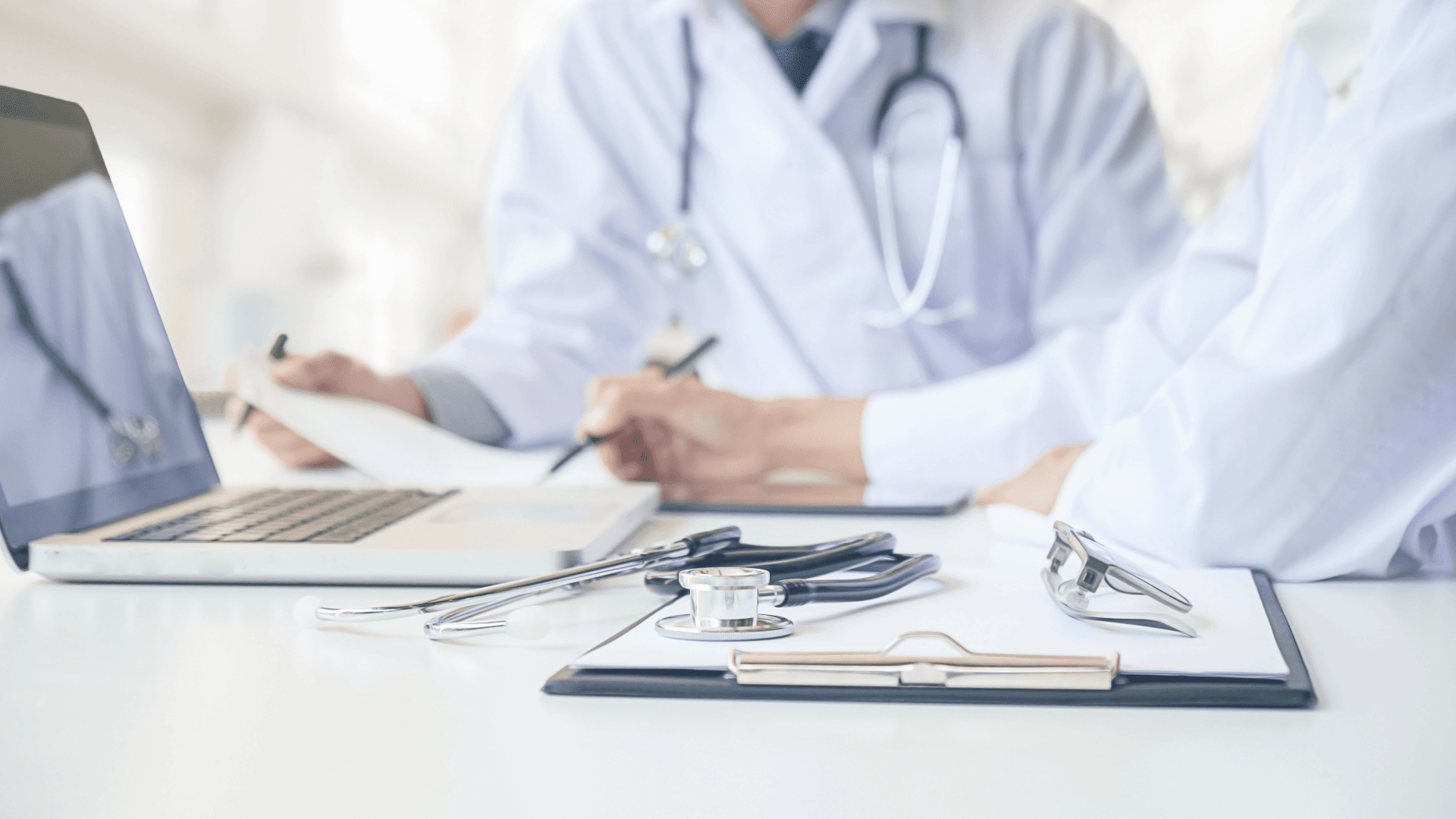 Doctors reviewing documents at a laptop with a stethoscope on the desk, symbolising the healthcare system