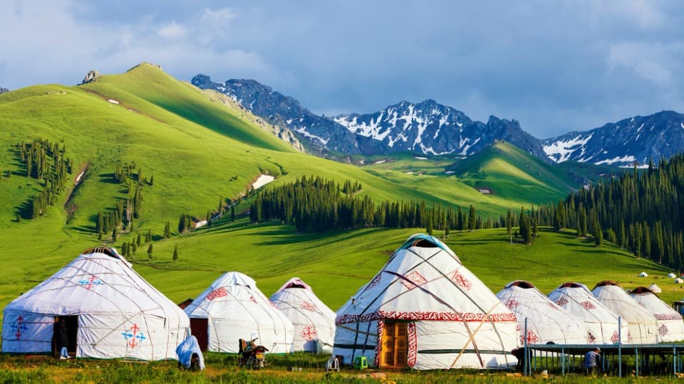 Traditional yurts in Mongolia’s green mountain landscape with snow-capped peaks in the background