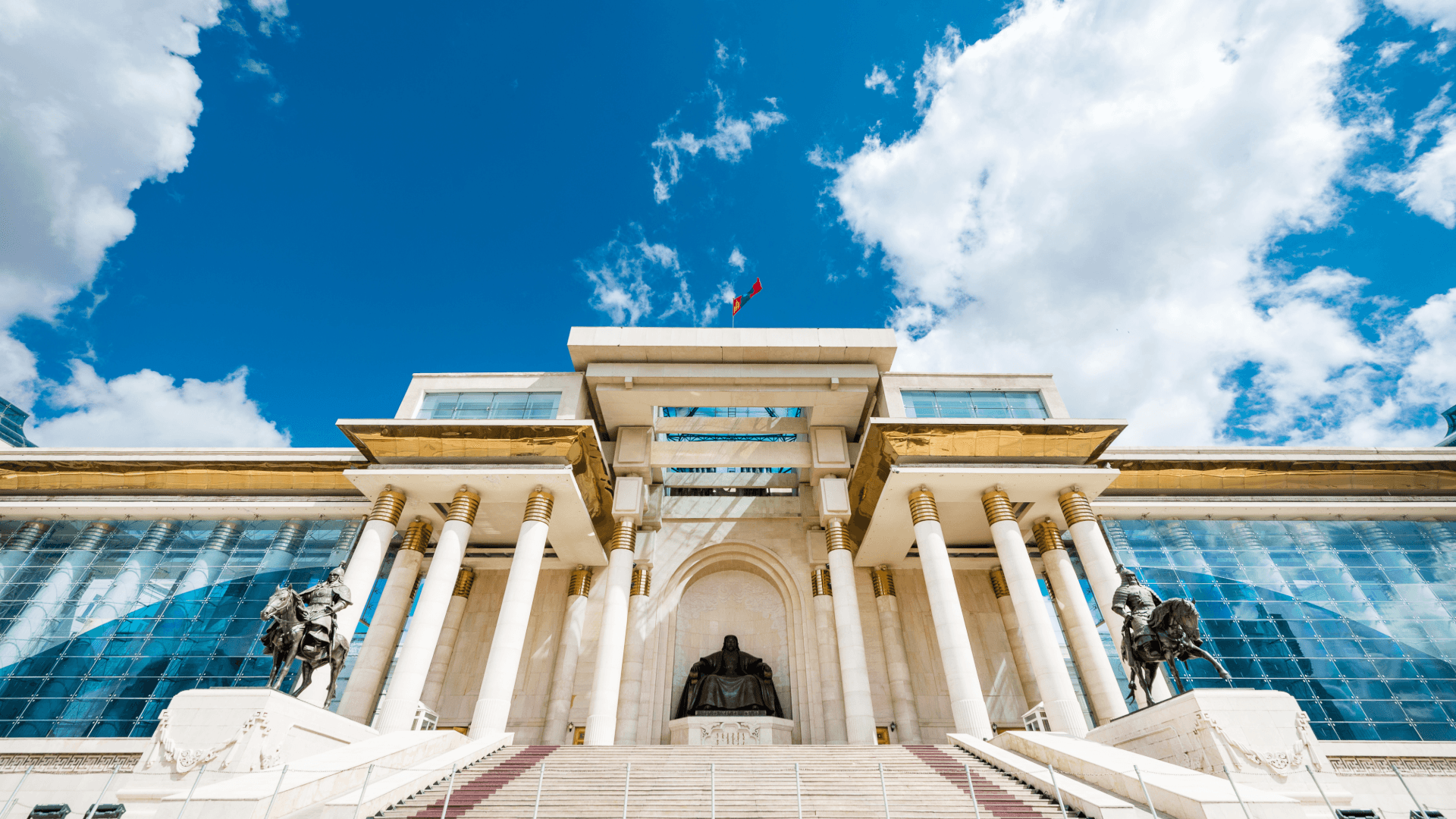 Monumental government building in Ulaanbaatar with columns, steps and Mongolian flag under a blue sky