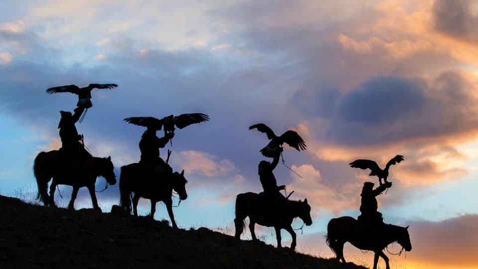 Silhouettes of Mongolian riders with hunting eagles at sunset in a wide open landscape