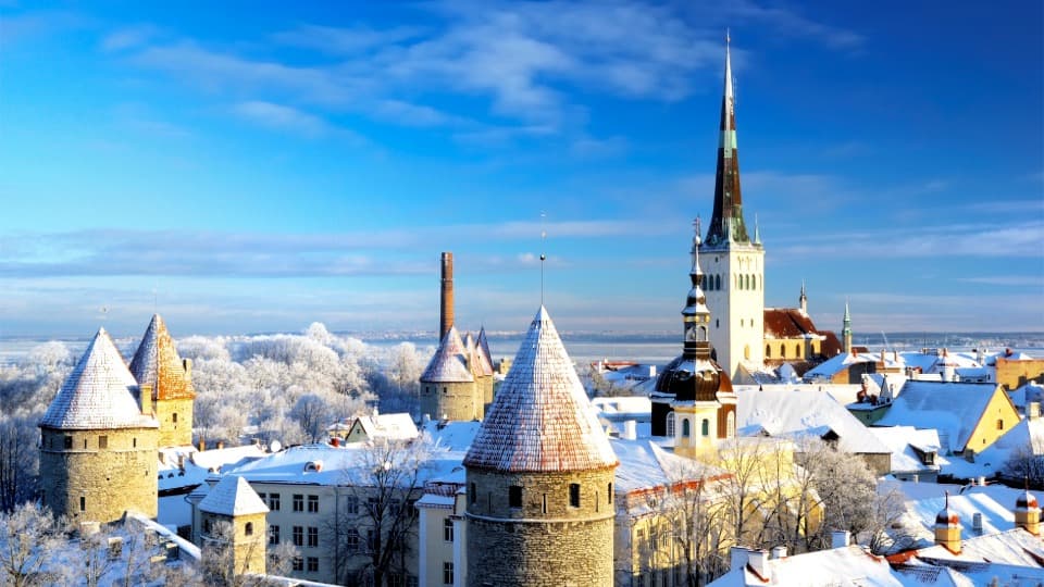 Snow-covered old town of Tallinn with church spire and historic towers under a blue winter sky