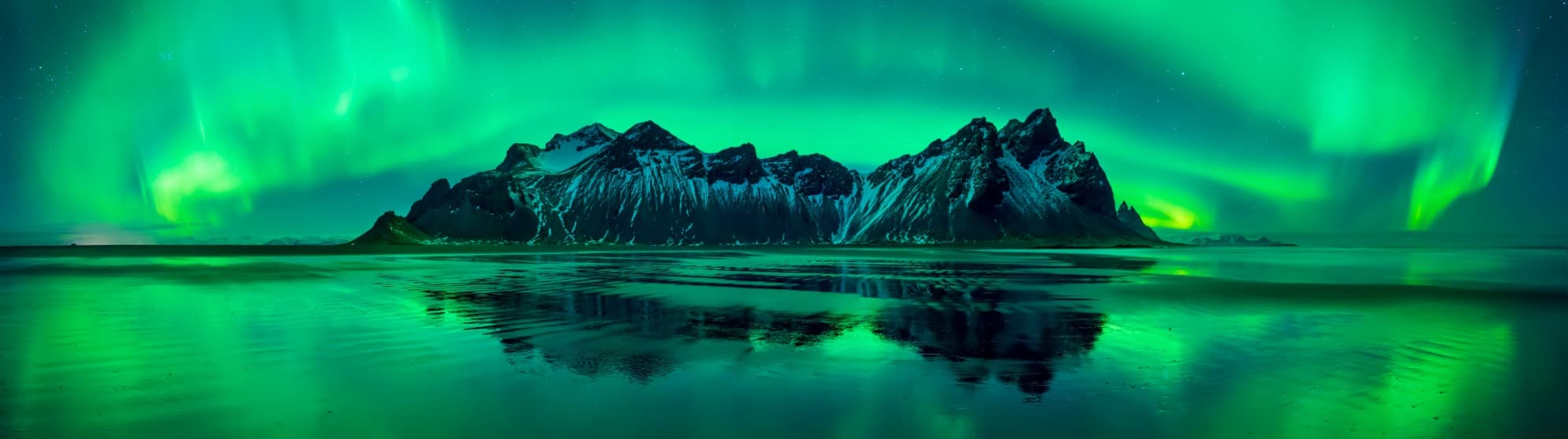 Northern lights over snow-covered mountains and reflective water in Iceland