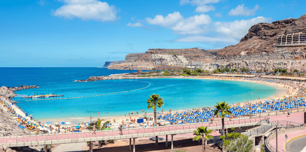 Bay in Spain with sandy beach, palm trees, turquoise sea and rocky coastal landscape