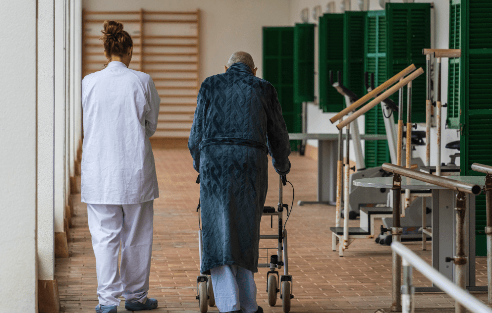 Care worker assisting an elderly person with a walker in a medical facility in Spain