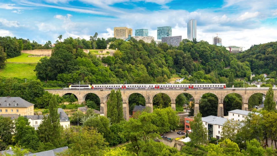 Free public transportation in Luxembourg: A train crosses the viaduct against the backdrop of the EU institutions and modern office buildings in Luxembourg City.