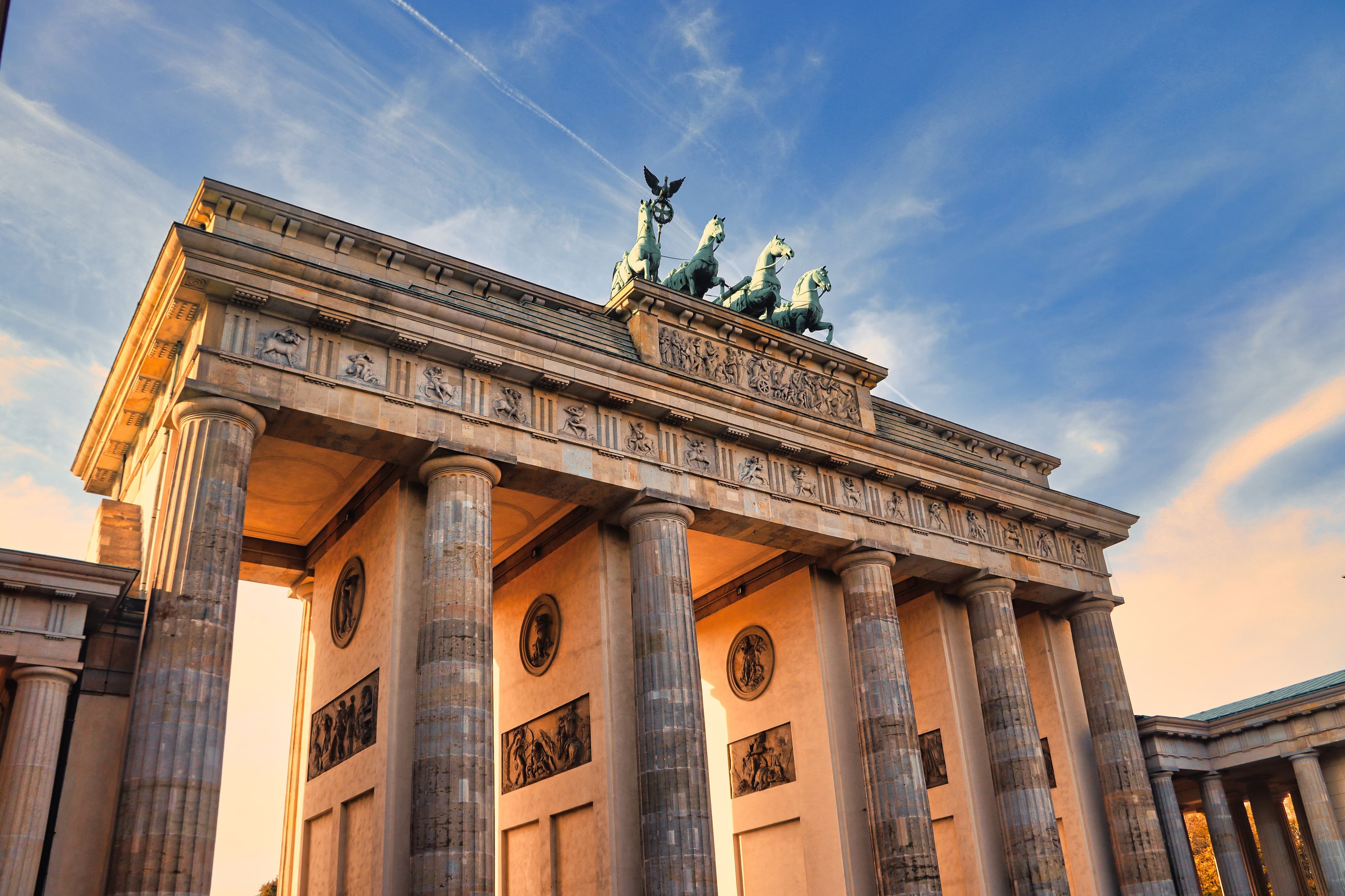 Brandenburger Tor in Berlin mit Quadriga im warmen Abendlicht vor blauem Himmel.