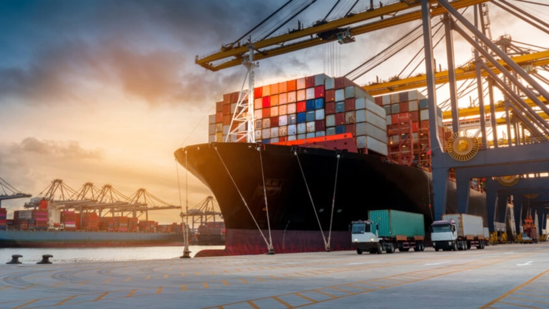 Container ship in port at sunset being loaded and unloaded by cranes and trucks