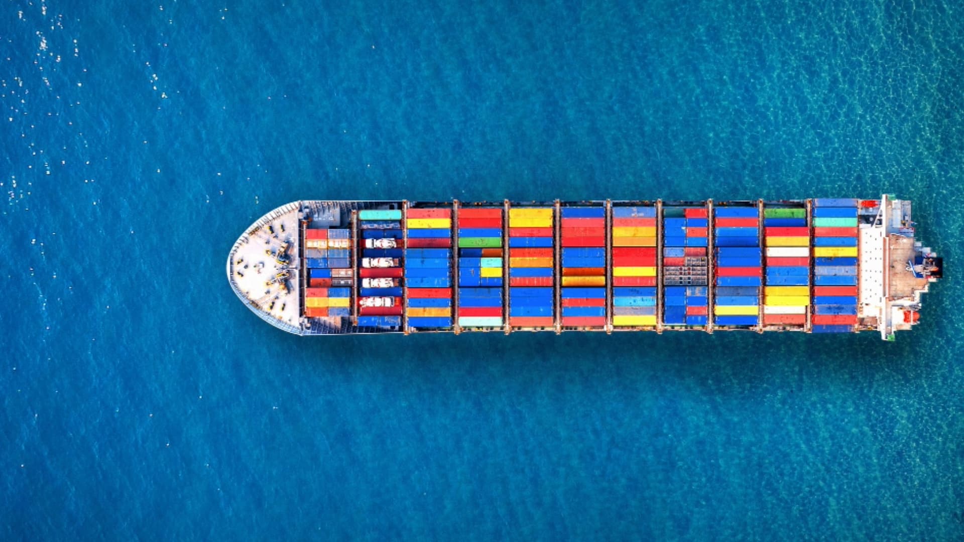 Aerial view of a large container ship loaded with colorful cargo containers sailing on the open sea.