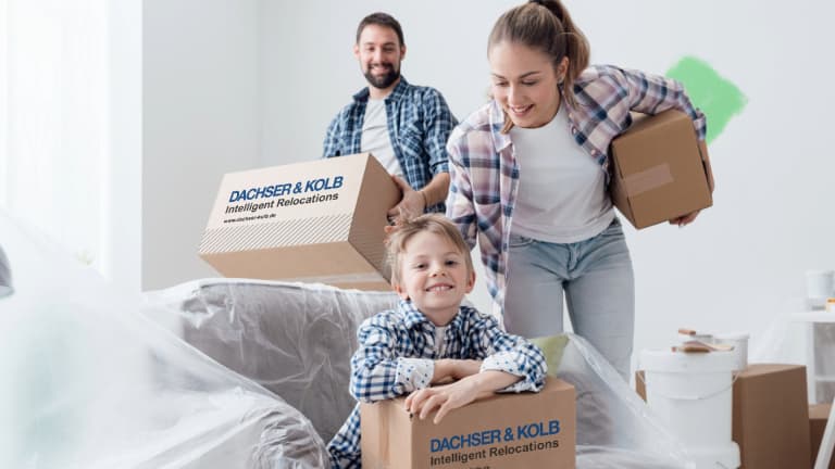 Eine glückliche Familie mit Kind trägt DACHSER & KOLB Umzugskartons beim Familienumzug in das neue Zuhause.