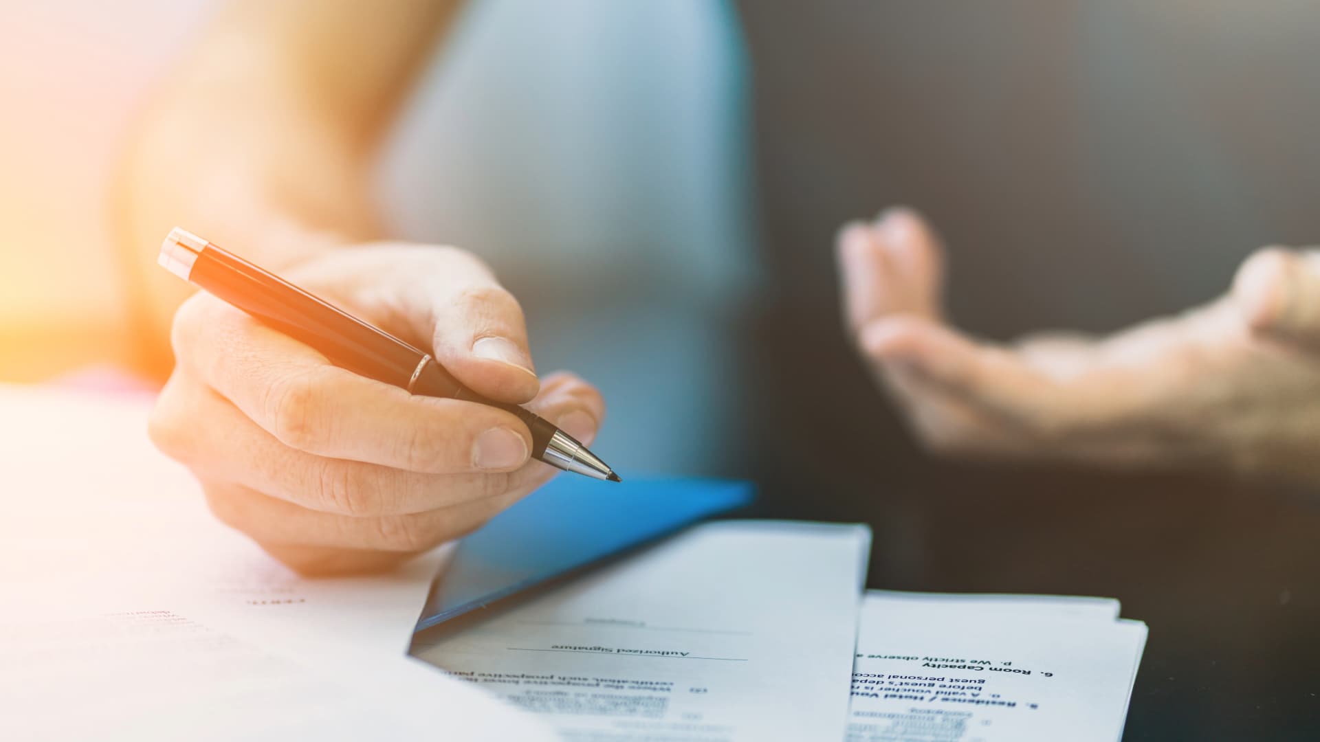 Hand signing documents, possibly for transit insurance. Person talking in the background.