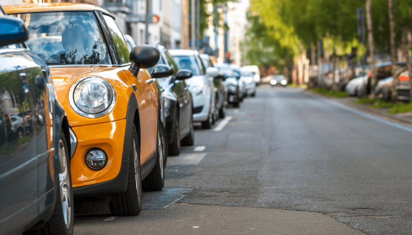 Several cars illegally parked on the roadside despite no-parking signs.