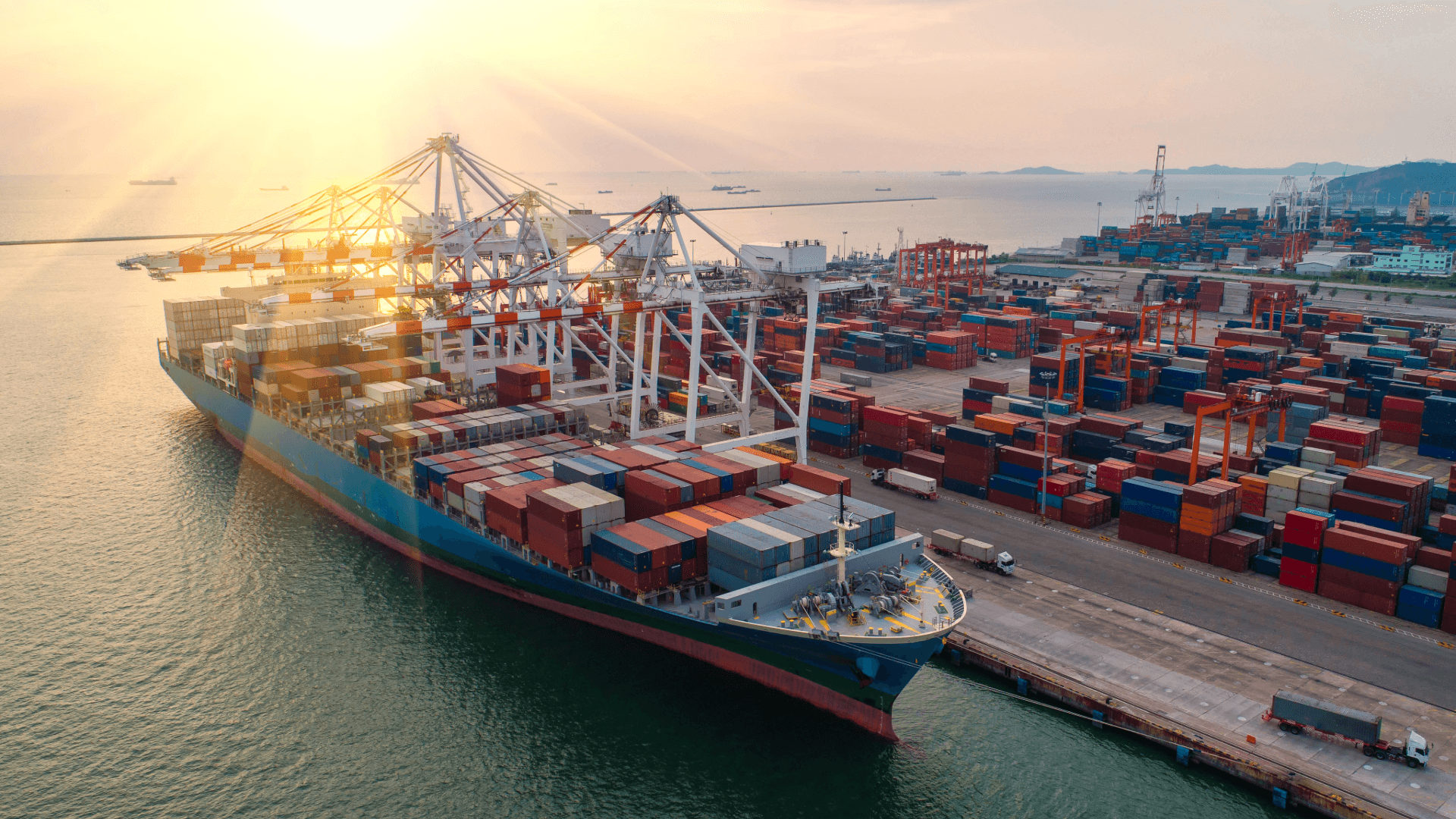 A large container ship in port, loaded with FCL containers. Cranes load cargo in the evening sun.