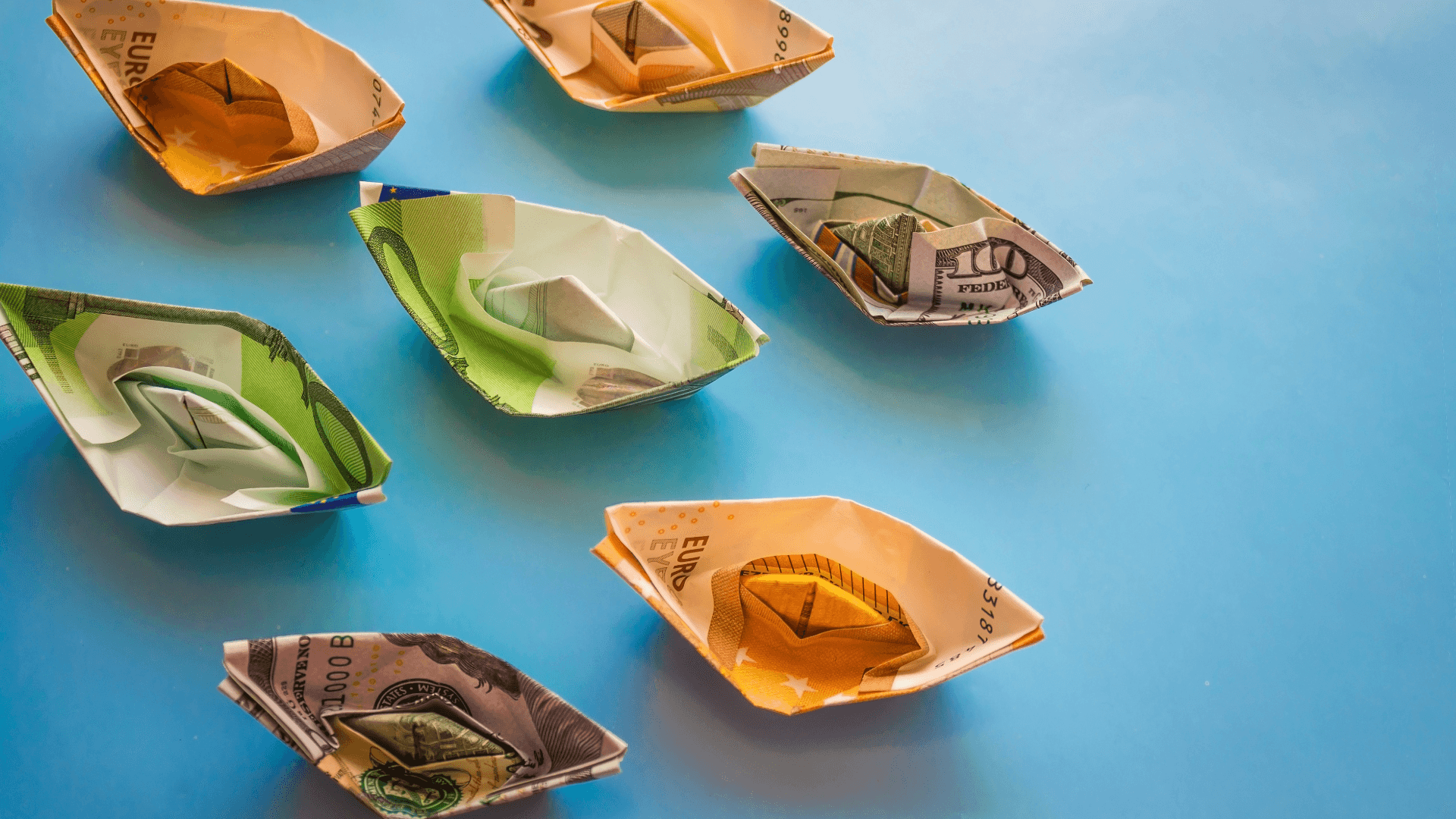 Paper boats folded from euro and dollar banknotes on blue background