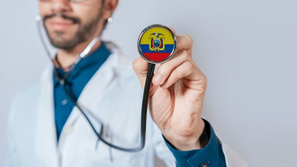 An Ecuadorian doctor holds a stethoscope with the national flag toward the camera as a symbol of Ecuador’s healthcare system.