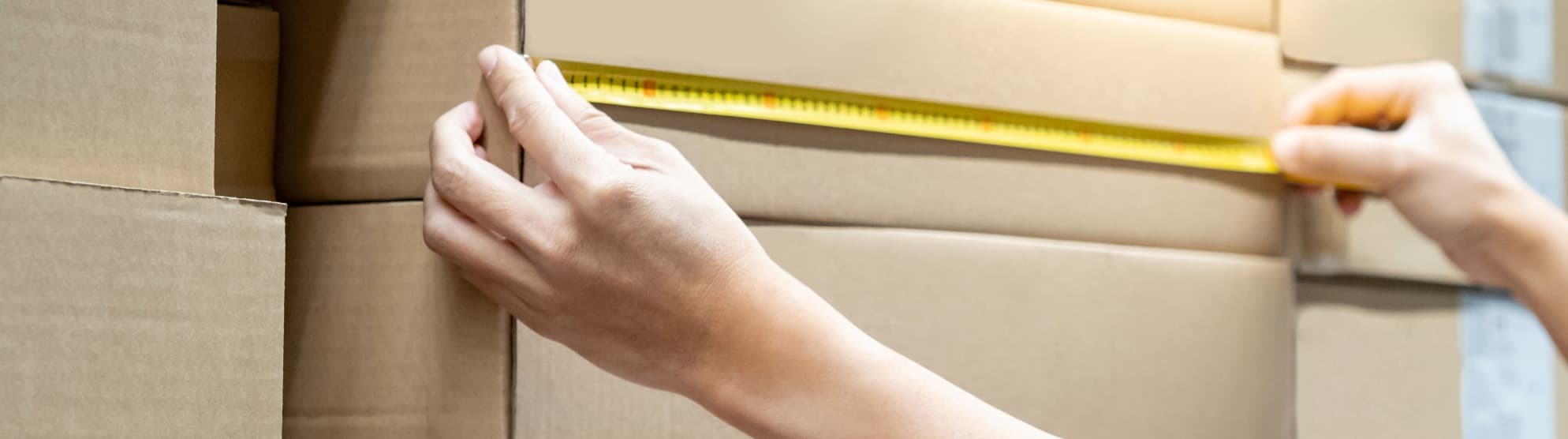 Person measuring a cardboard box with tape measure to calculate transport volume