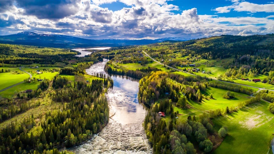 Aerial view of a Swedish landscape in summer, featuring a river, forests, and meadows