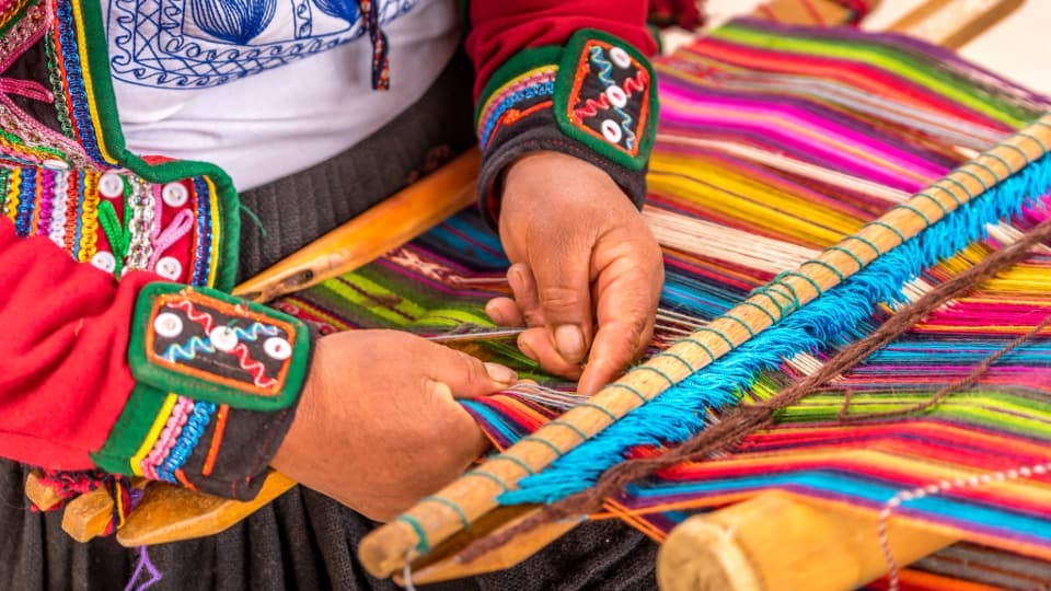 Ein Peruaner in traditioneller Kleidung webt einen bunten Umhang