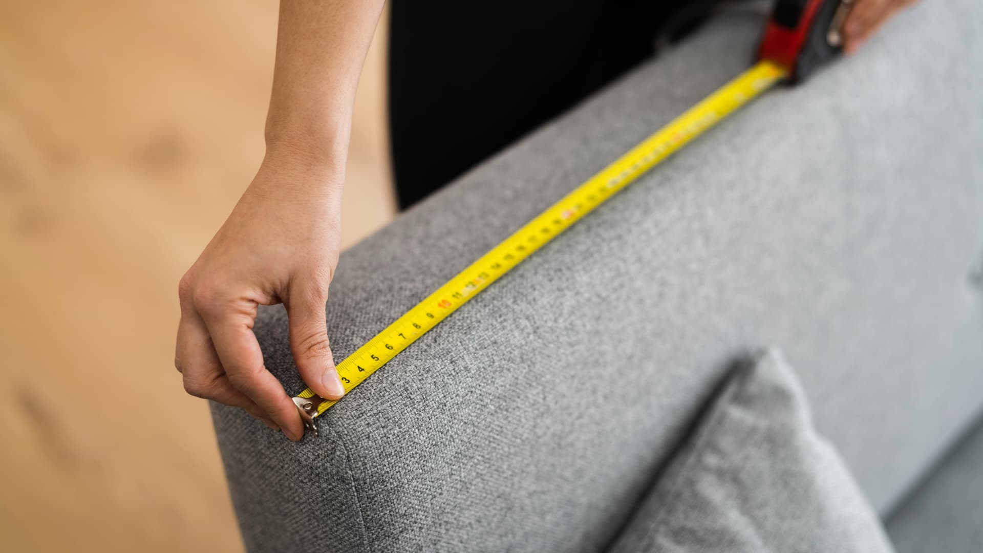 A person measuring a sofa with a tape measure to determine its volumetric weight for transport and facilitate moving planning.