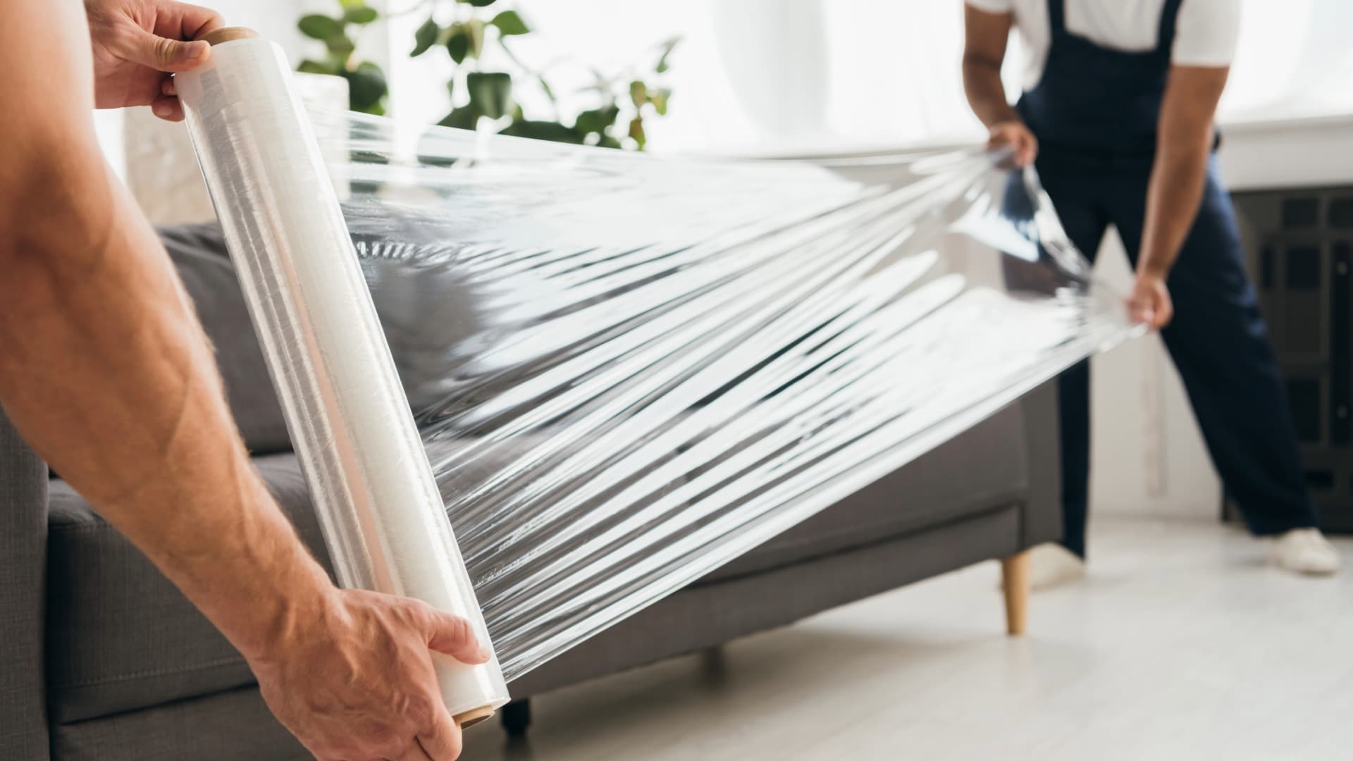 Zwei Fachkräfte verpacken eine Couch mit transparenter Schutzfolie für einen Umzug.