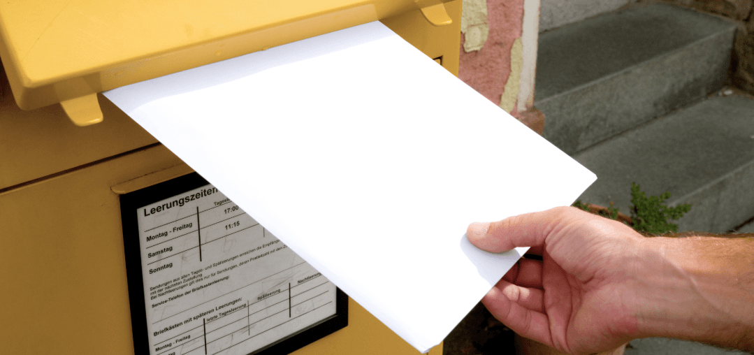 Hand wirft Brief in gelben Postkasten – Symbolbild für das Einreichen eines Nachsendeauftrags bei der Post.