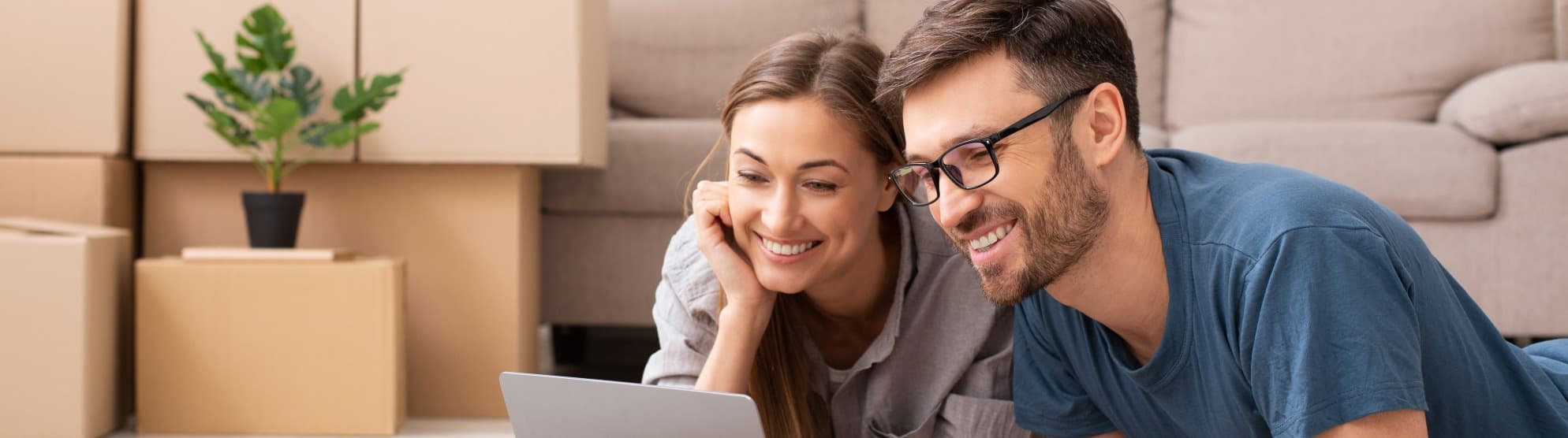 Couple planning their move on a laptop in front of moving boxes in the living room