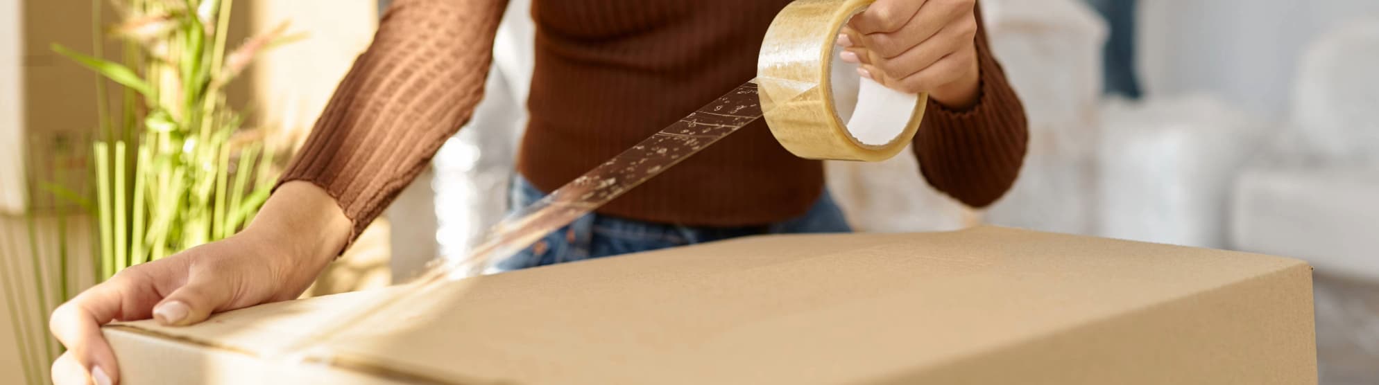 Close-up of a person sealing a moving box with tape, typical for a "Packed by Owner" (PBO) move.