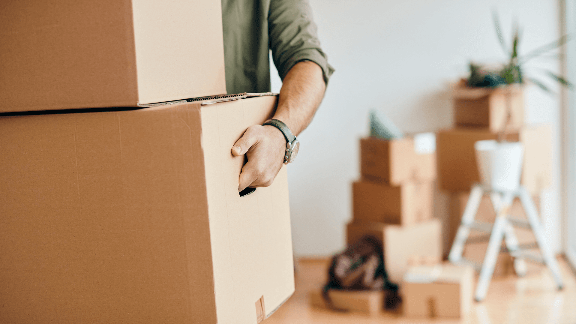 Person carrying moving box indoors – moving boxes in the background, symbol of relocation and organization