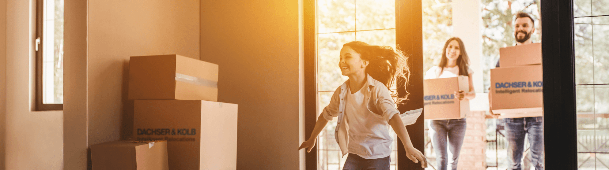 Happy family during private move – child runs joyfully into new home while parents carry moving boxes inside.