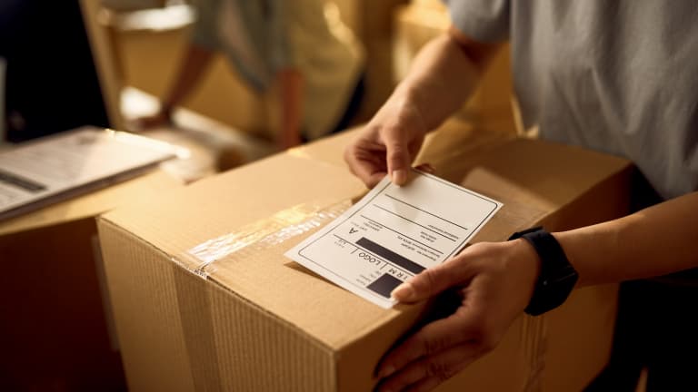 Nahaufnahme einer Person, die ein Retourenlabel auf ein Paket klebt – Symbol für schnellen Retourenservice.