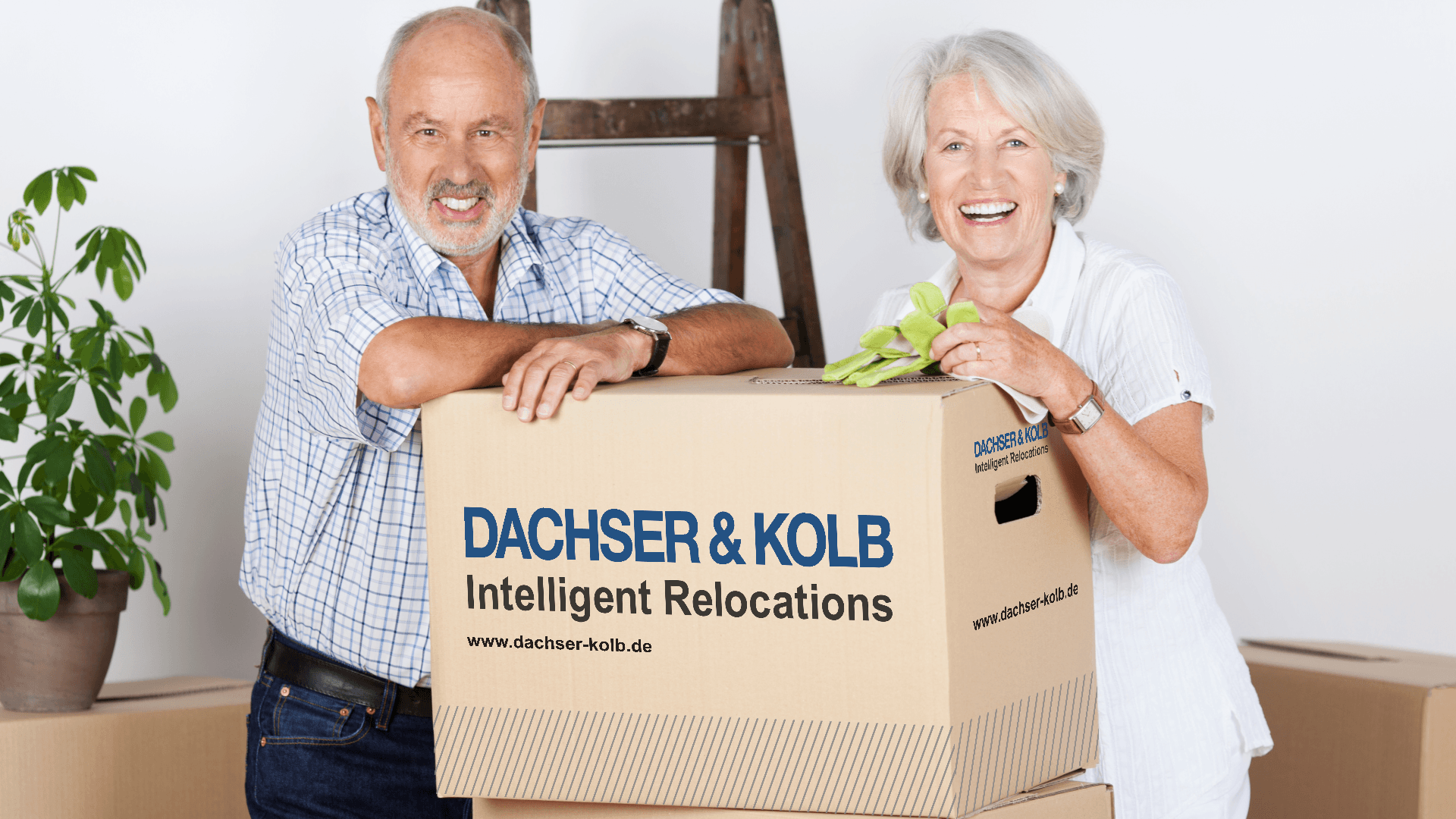 Smiling senior couple with moving box – stress-free senior relocation to upscale residences with DACHSER & KOLB