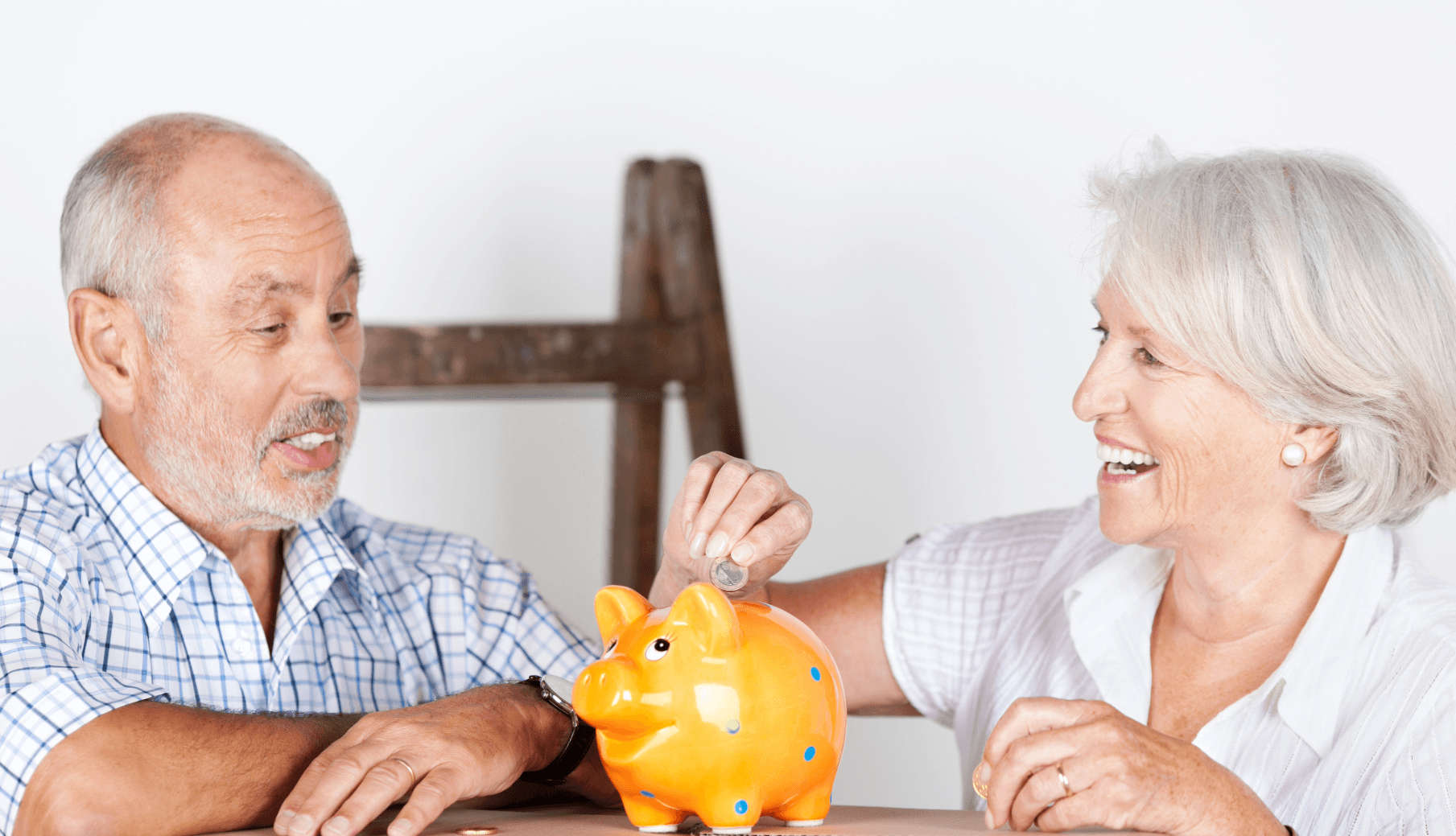 Senior couple saving money for upscale senior relocation – smiling with piggy bank