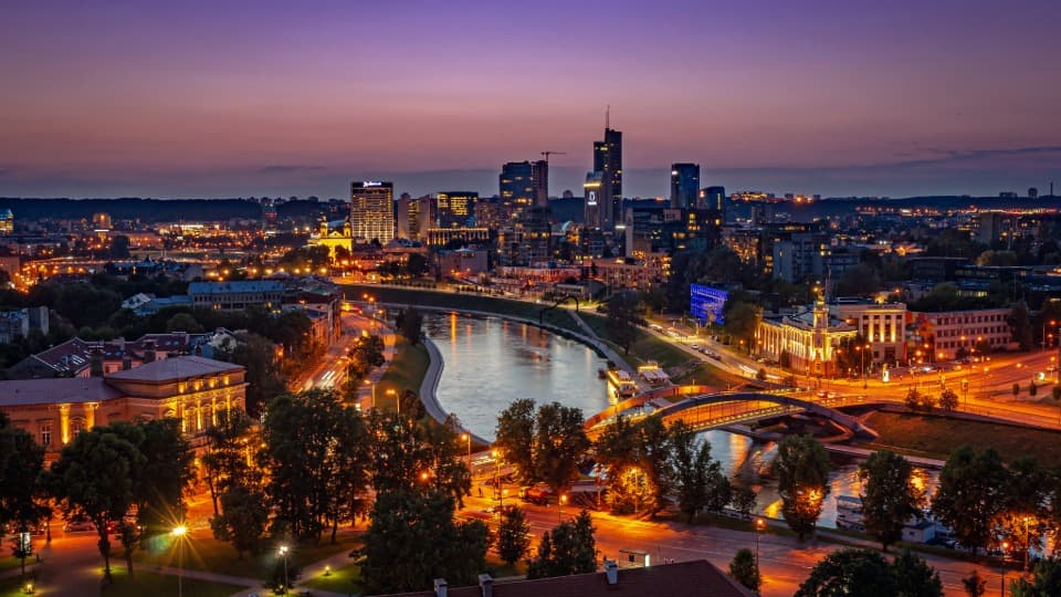 The night skyline of Vilnius, with illuminated skyscrapers along the Neris River – a symbol of stability and security in modern Lithuania.