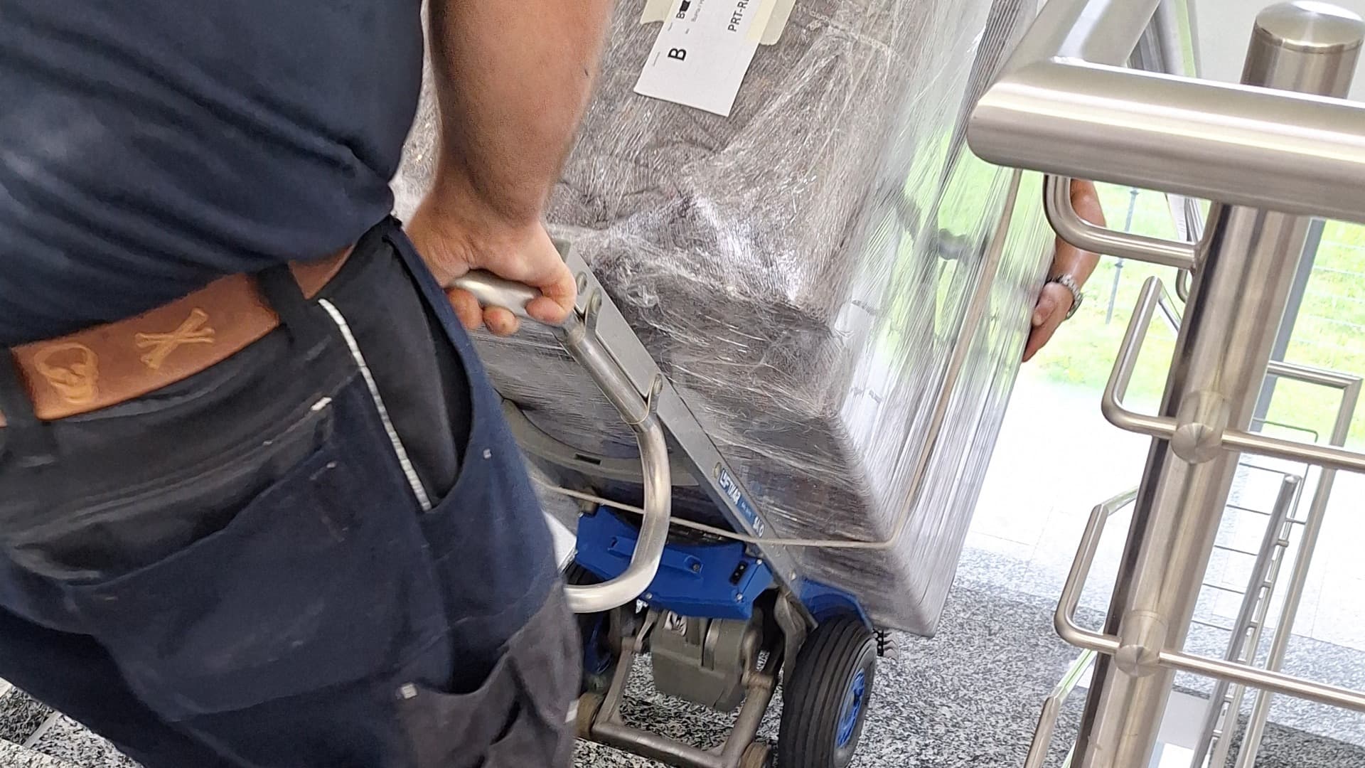 Mitarbeiter transportiert verpacktes Möbelstück mit einem Treppensteiger sicher eine Treppe hinauf.