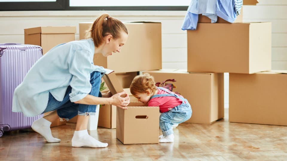 Eine Mutter packt mit ihrem Kleinkind Umzugskartons für einen deutschlandweiten Familienumzug.