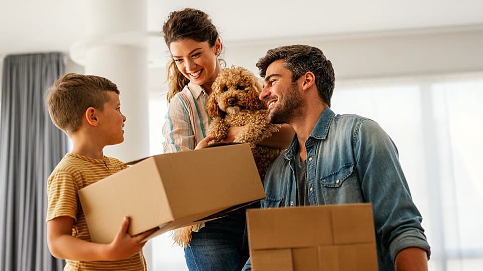 Eine glückliche Familie mit Kind und Hund hält Umzugskartons in der neuen Wohnung.