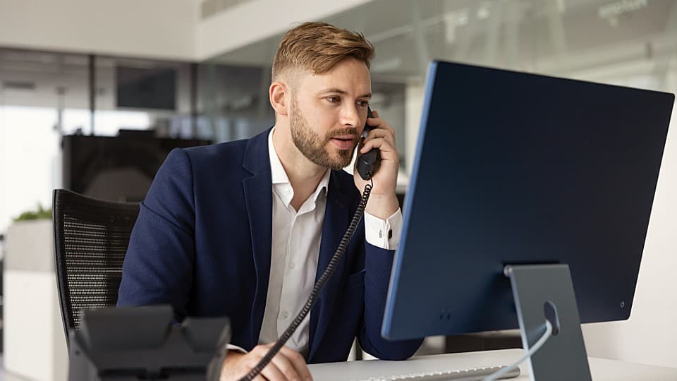 Ein professionell gekleideter Mitarbeiter im Büro berät Kunden am Telefon und PC zum Umzugsservice per Seefracht.