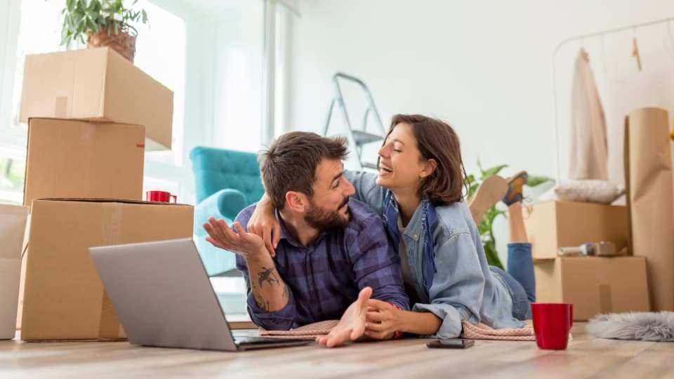 A happy couple uses a laptop to digitally plan their professional packing services and furniture assembly for a move with DACHSER & KOLB.