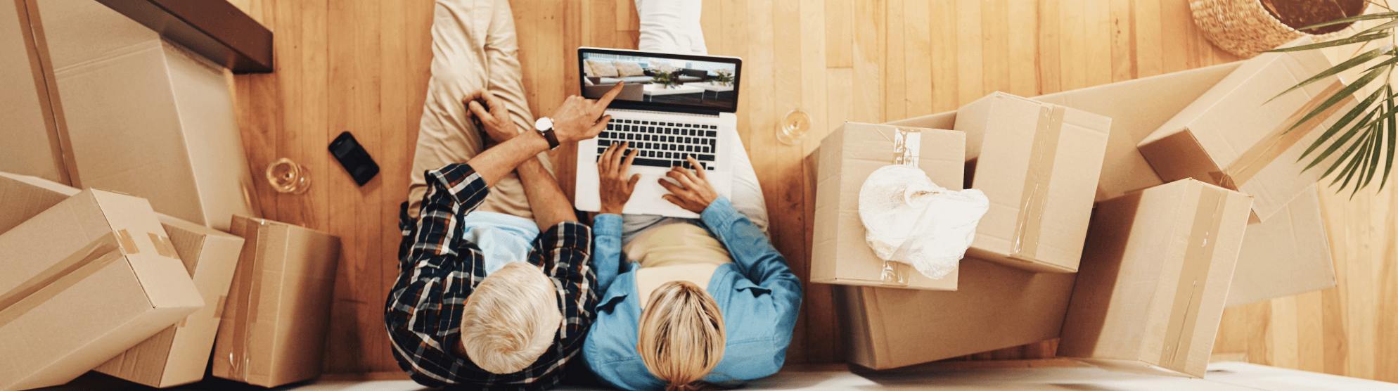 Älteres Paar berechnet Umzugskosten am Laptop, umgeben von Umzugskartons in neuer Wohnung