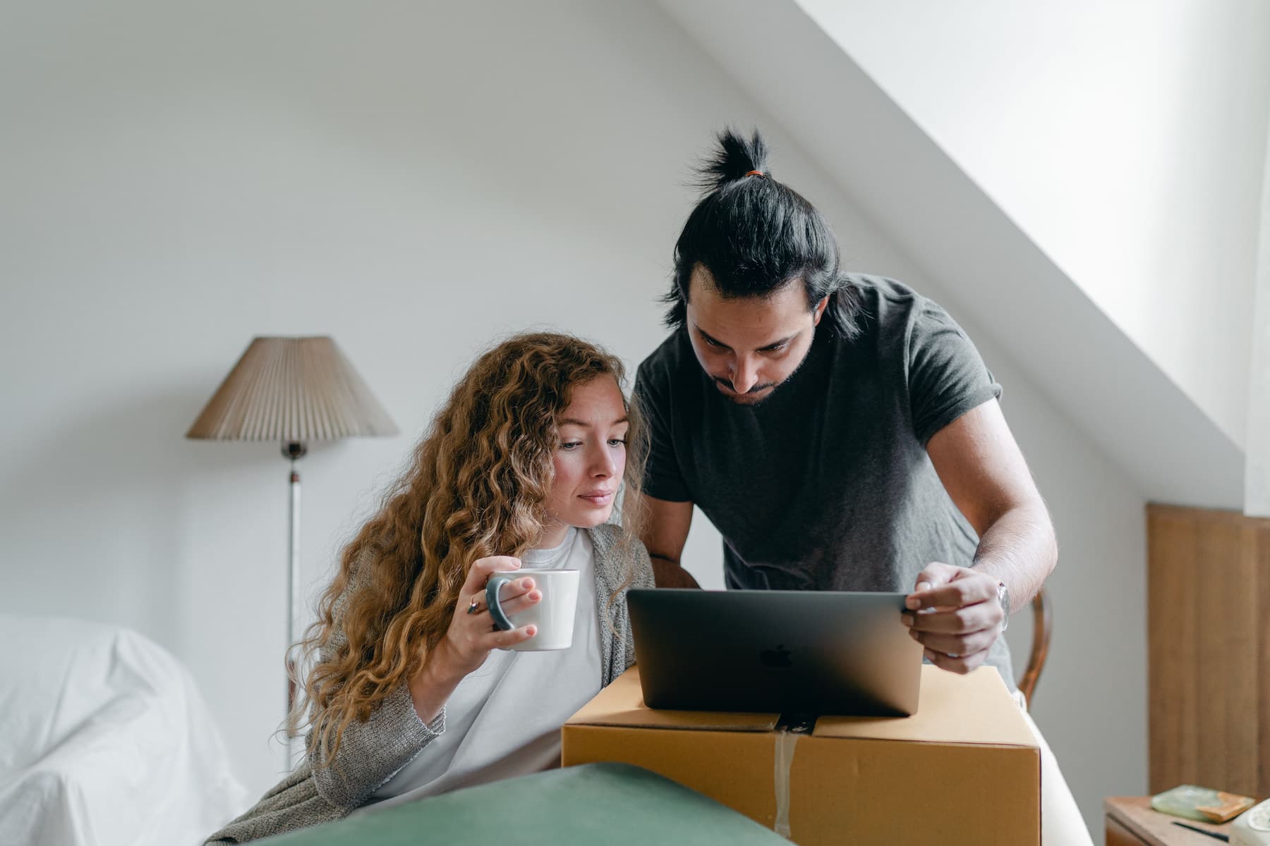 A couple looks at a laptop resting on a moving box.