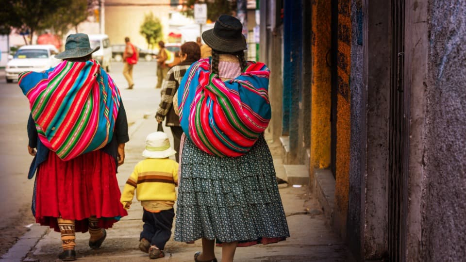 Two Bolivian women in traditional dress walk down a street with a child