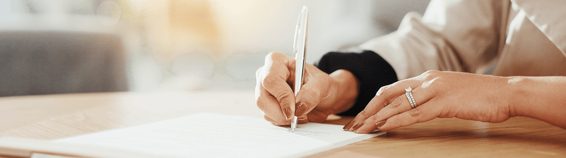 Nahaufnahme einer Hand, die eine Wertgutliste unterschreibt; Fokus auf Stift und Dokument.