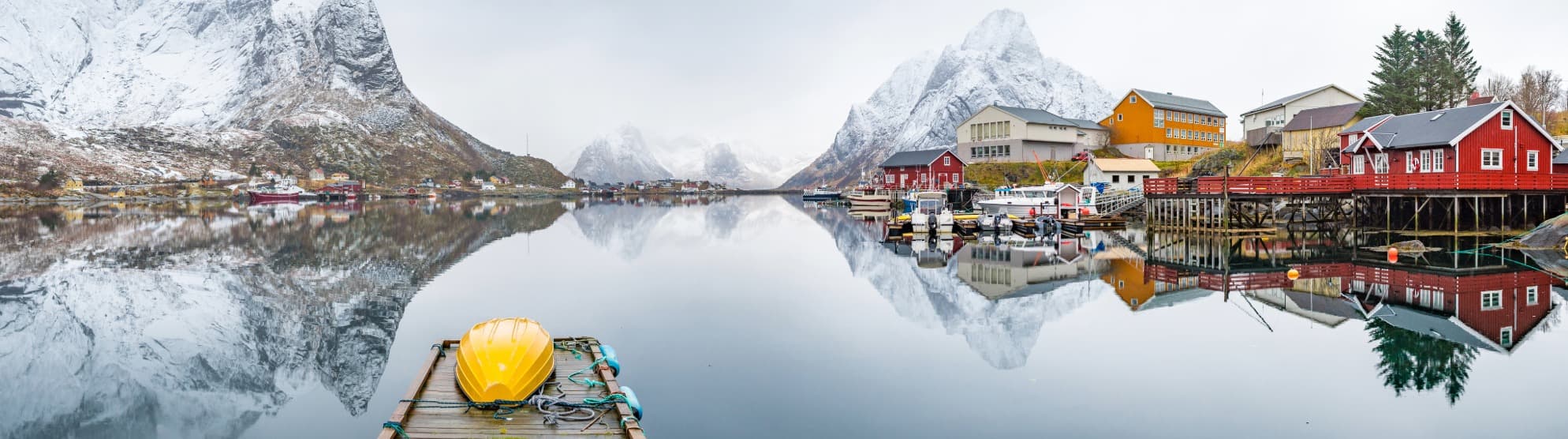 Norwegian fjord village with snow-covered mountains and reflections on calm water