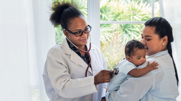 Ärztin hört ein Kind auf dem Arm der Mutter mit dem Stethoskop ab.