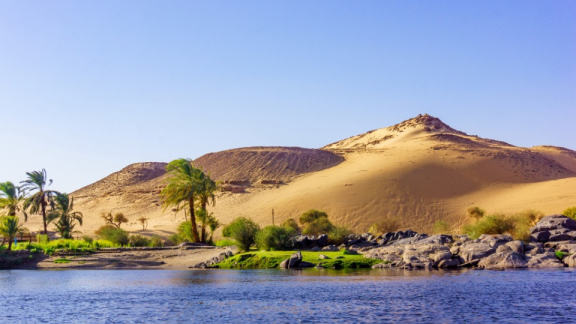 A landscape in Egypt with palm trees, the Nile, and the desert in the background