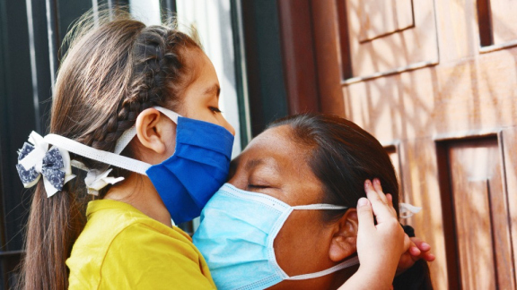 Healthcare in Peru: A girl wearing a mask hugs another masked person.